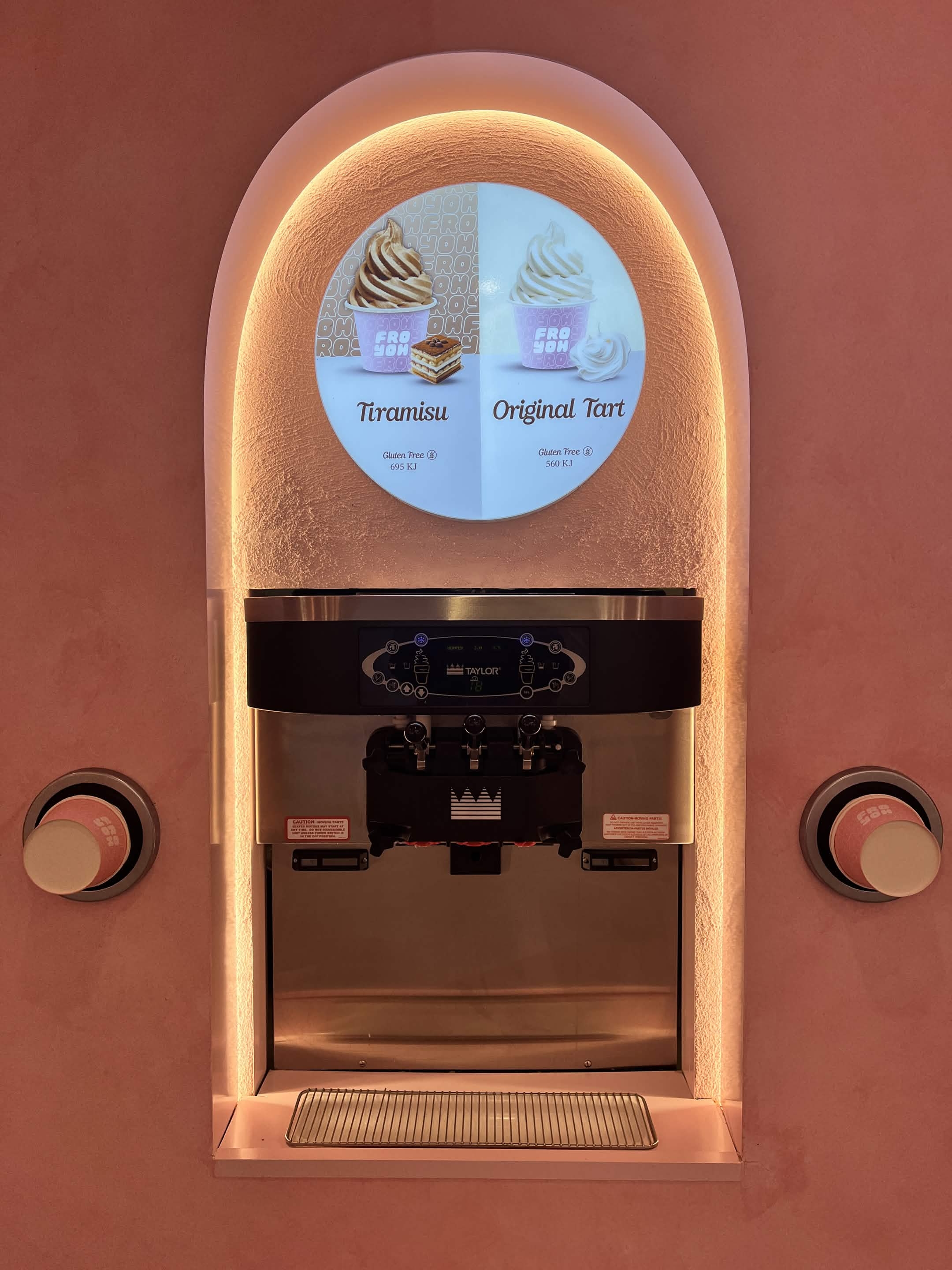 Soft-serve machine under a pink arched niche with a Tiramisu and Original Tart flavour sign