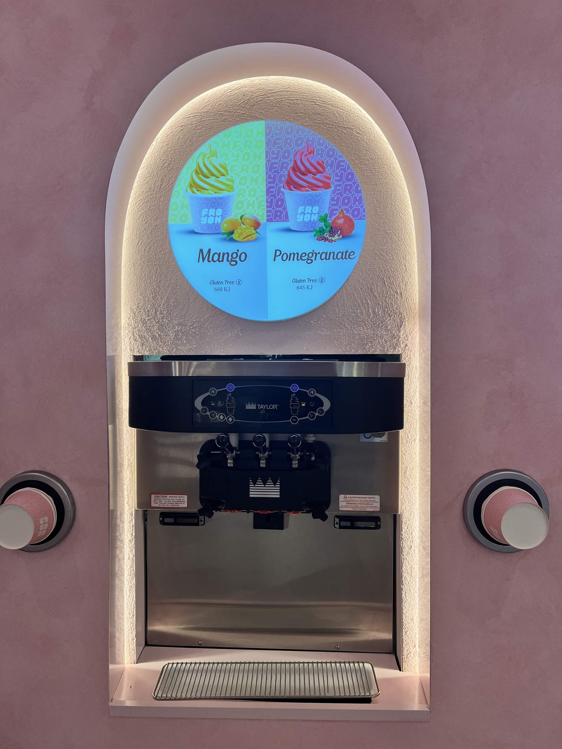 Soft-serve machine under a pink arched niche with a Mango and Pomegranate flavour sign
