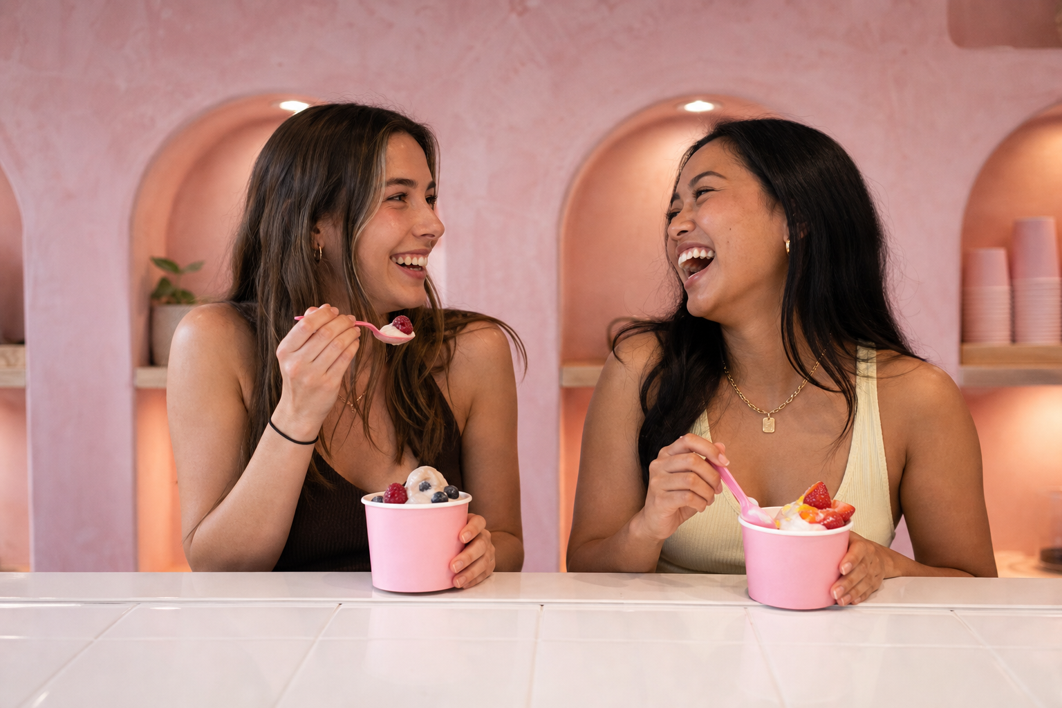 Two friends laughing over frozen yogurt cups at the Fro Yoh counter
